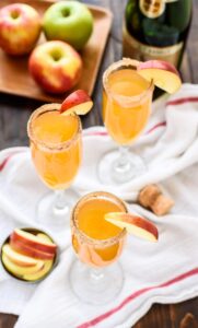 Champagne glasses full of apple cider mimosas garnished with apple slices on a white table cloth