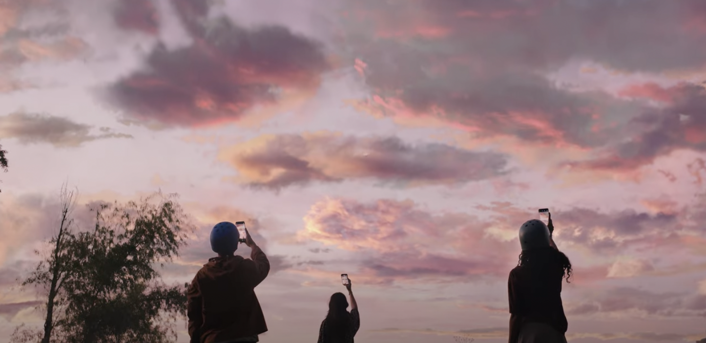 Three people hold phone cameras to the dusk sky.