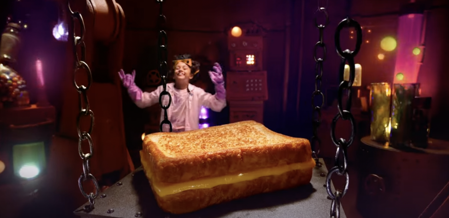 A child appears as a mad scientist with a giant grilled cheese sandwich in a lab