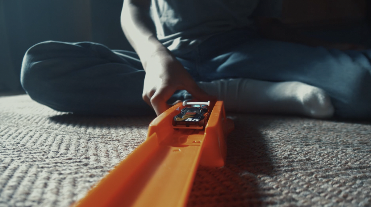 A child sets up a toy car on an orange Hot Wheels track