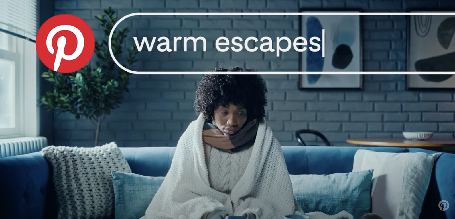 A woman is wrapped in a blanket on a couch searching "warm escapes"