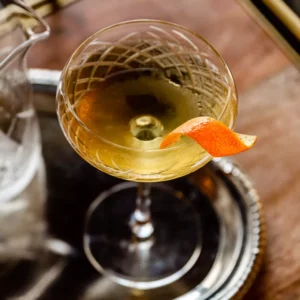 A light golden colored cocktail with an orange twist 