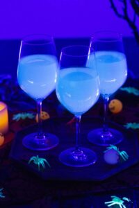 Three wine glasses full of a tonic cocktail glow under a blacklight