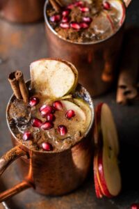 A drink in a copper mule mug garnished with pomegranate and cinnamon sticks