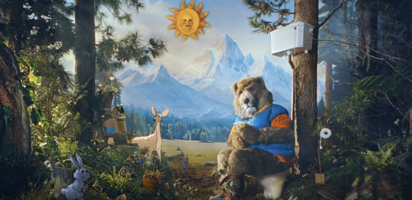 A person in a bear suit wearing a hoodie sits on a toilet in a staged woodland setting with cartoon deer and rabit