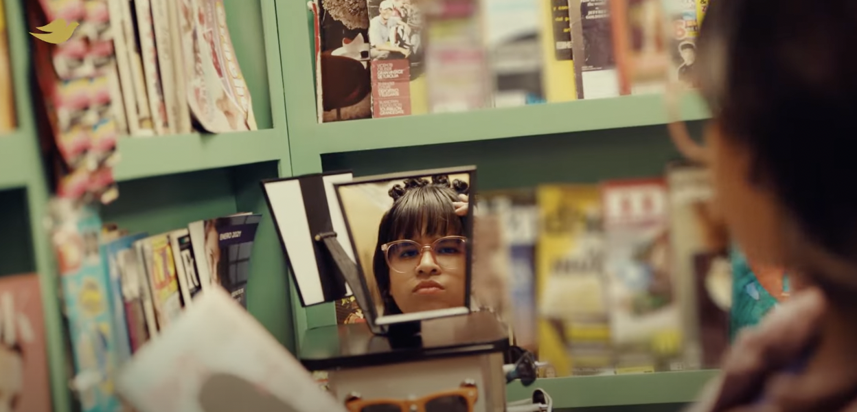 A woman looks into a mirror in a magazine newsstand and considers her alternative hairstyle