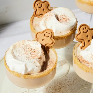 Three martinis topped with whipped cream and gingerbread man cookies